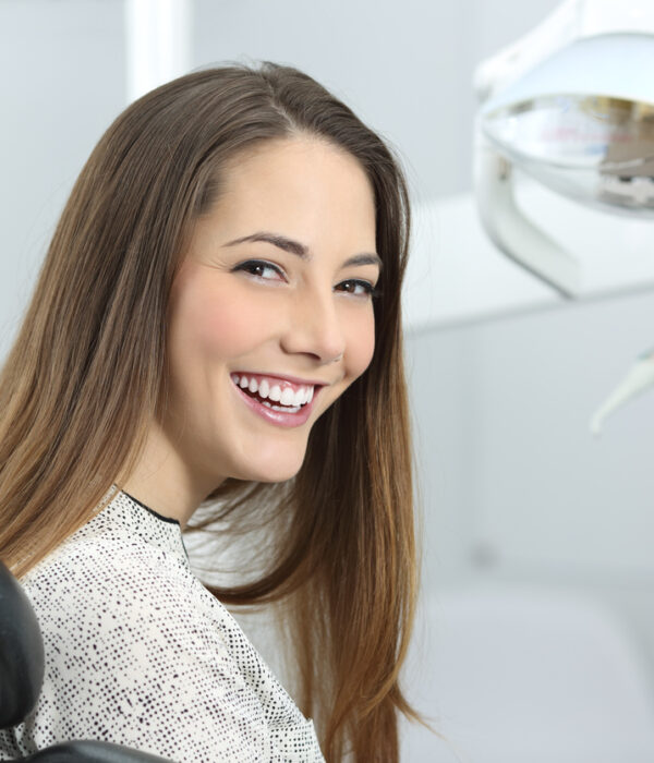 Satisfied dentist patient showing her perfect smile after treatment in a clinic box with medical equipment in the background